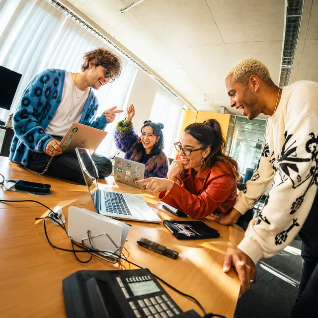 Creative team laughing around laptops at an office table